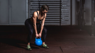 Long-haired person in dark gym lifting kettlebell