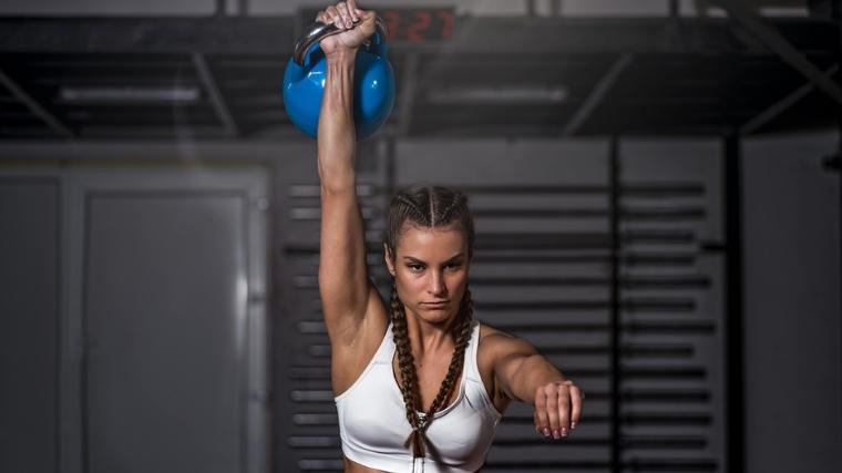 The woman performs a jerk with kettlebells