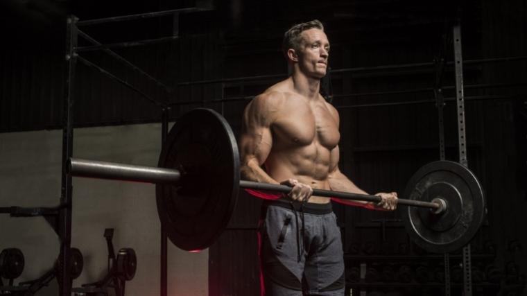 Muscular man curling a loaded barbell with both hands inside of the gym