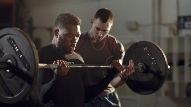 A person twists a barbell while another person trains him through a rep