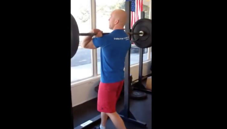 man in gym unracking barbell and preparing to squat