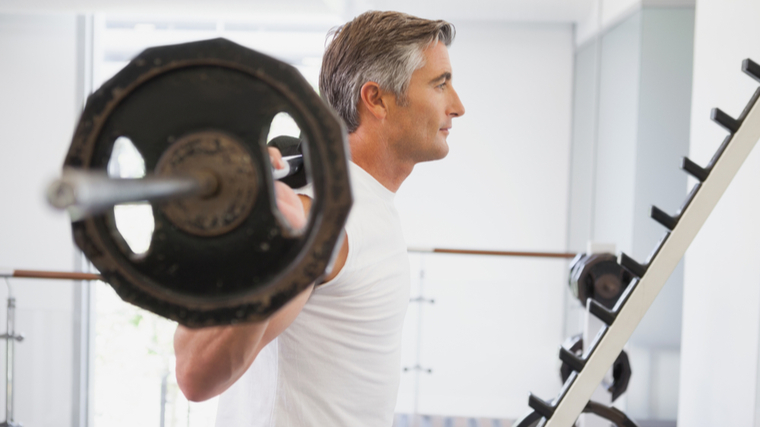 older man in gym with barbell on back preparing to squat