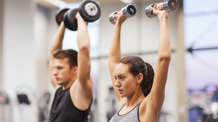 Man and woman exercising in gym pressing dumbbells overhead