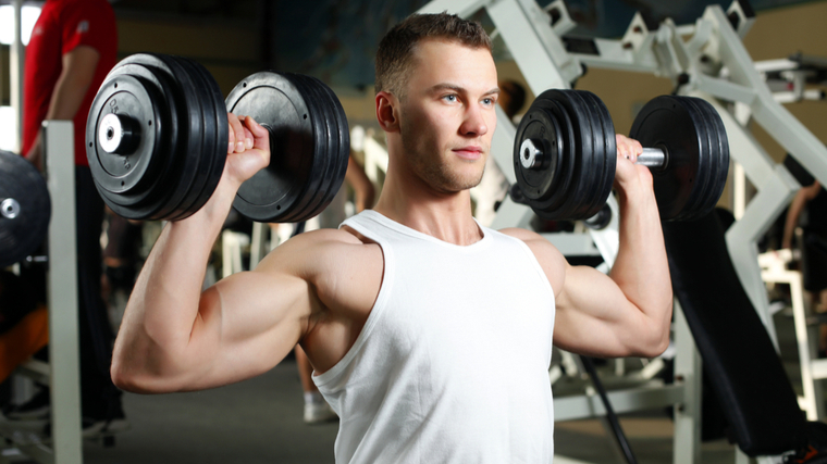 Muscular man holding dumbbells near shoulders