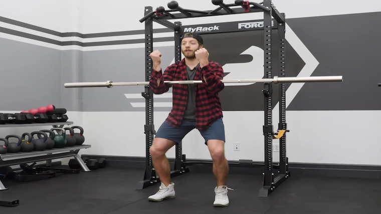 Man in gym squatting with barbell in arms