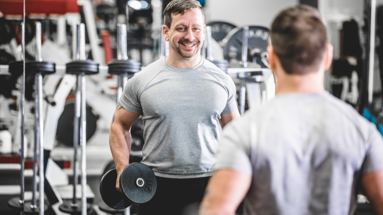 Man in gym holding dumbbells looking in mirror