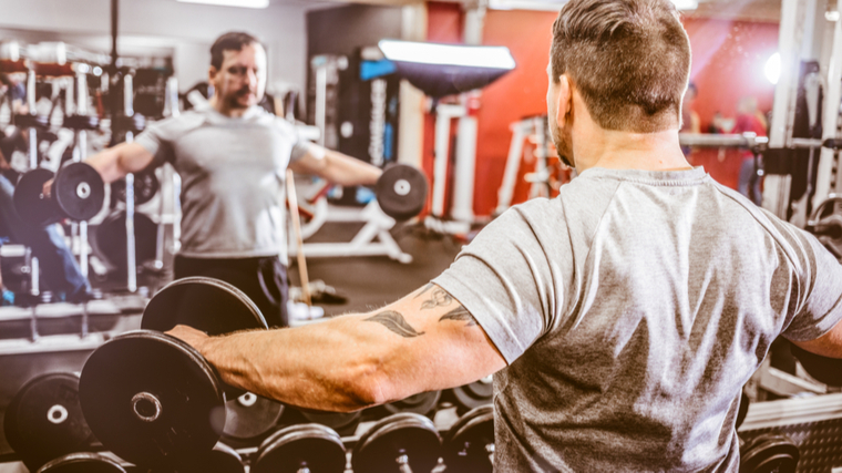 Man in gym performing shoulder exercise looking in mirror
