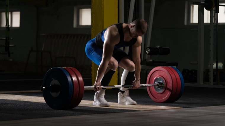 Athlete in dark gym preparing to lift barbell