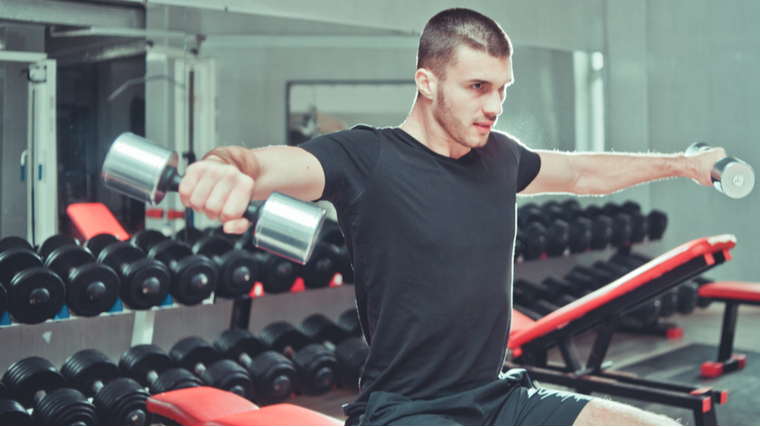 Man in gym holding dumbbells in air