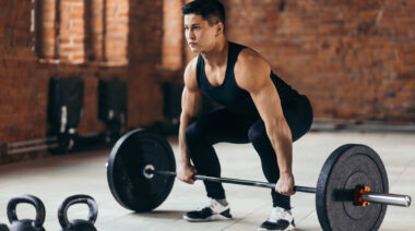 Man in bright room preparing to lift barbell from floor