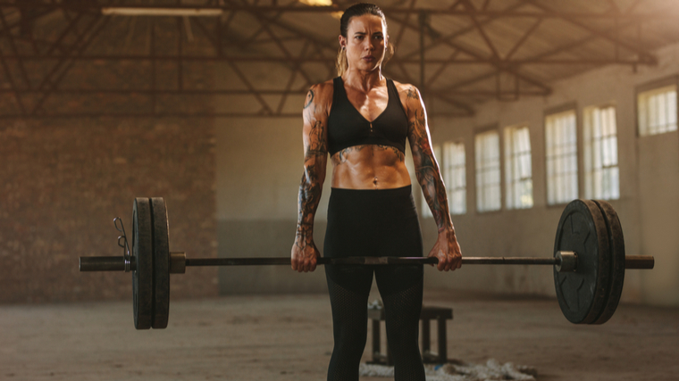 Muscular woman with tattoos holding heavy barbell