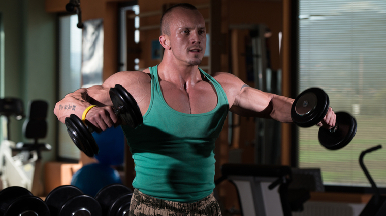 Muscular man in gym performing dumbbell side raise