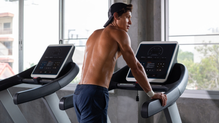 Shirtless man in gym standing on treadmill