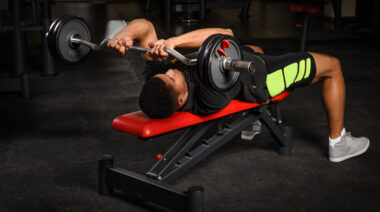 Man lying on flat bench performing barbell triceps exercise