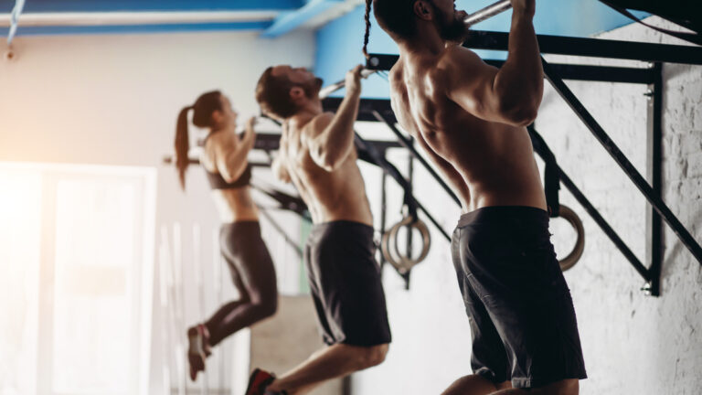 Three people performing pull-ups on wall-mounted bars.