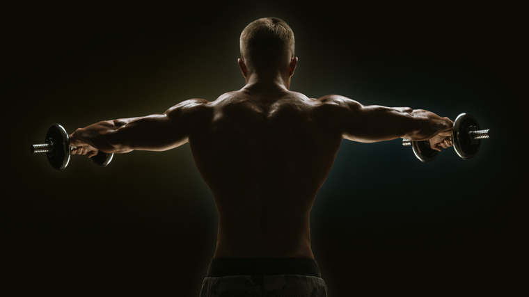 Bodybuilding in dim light performing dumbbell shoulder raise