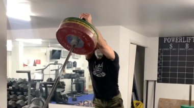 Muscular man in gym performing overhead barbell exercise