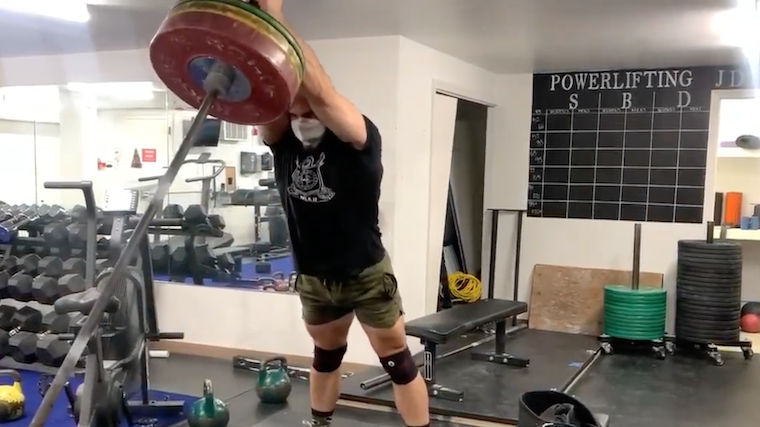 Muscular man in gym performing overhead barbell exercise