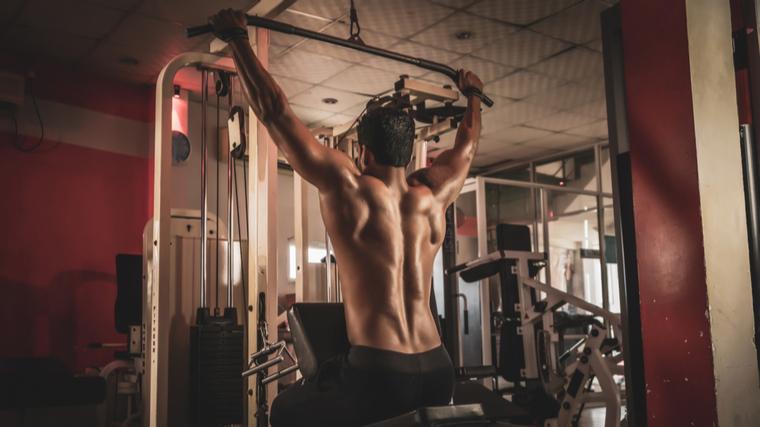 Muscular man performing lat pulldown in gym