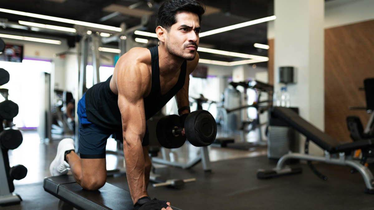 Muscular man in gym rowing dumbbell