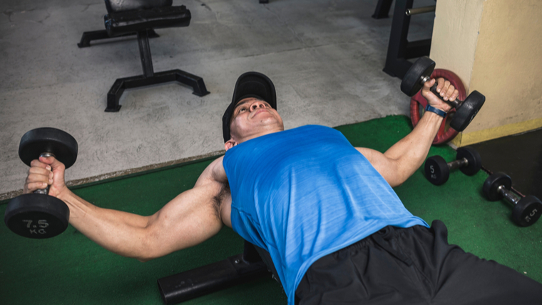 Man in gym stretching chest with dumbbells
