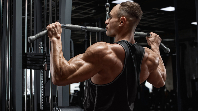 Muscular man performing back exercise on pulldown machine