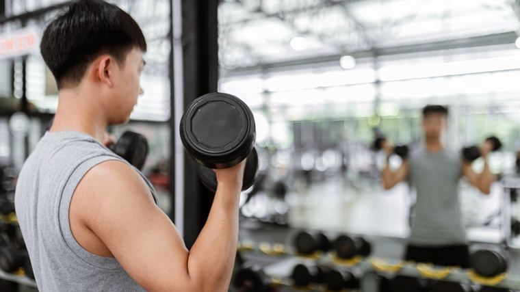 Man in gym performing dumbbell curl in mirror