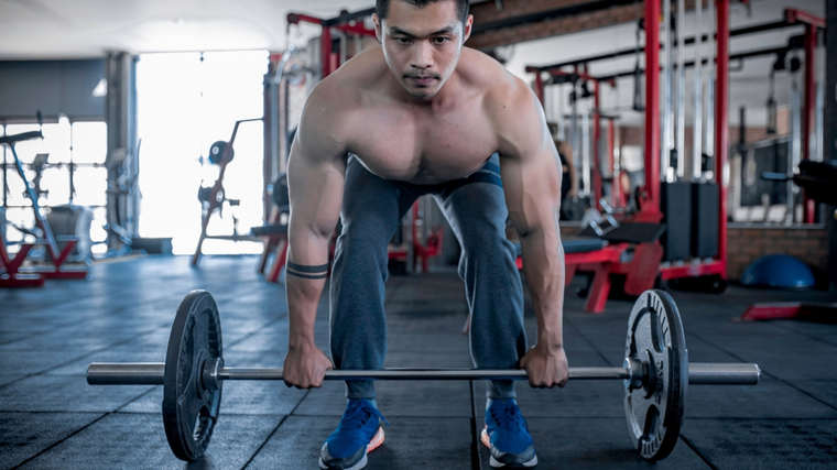 Muscular man in gym bending down to grab barbell