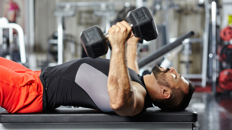 Man in gym performing dumbbell exercise on bench