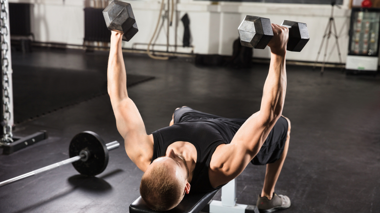 Man in gym on flat bench lifting dumbbells 