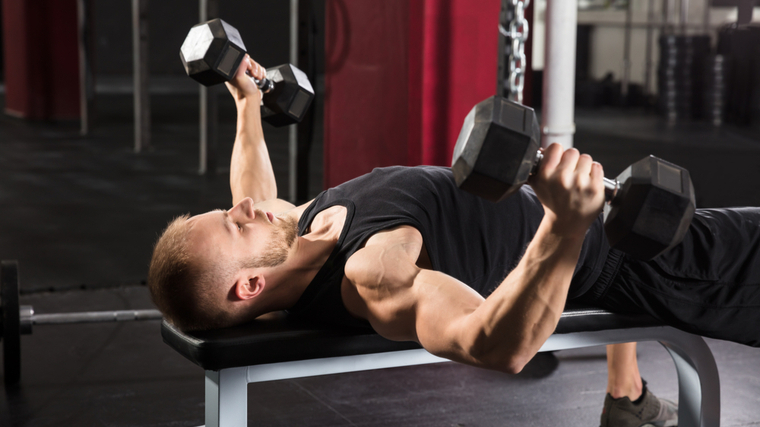 Man on bench in gym lowering dumbbells