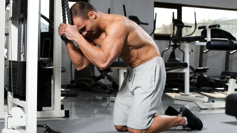 Muscular man kneeling in gym performing ab exercise