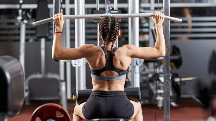 Muscular female fitness model exercising on a lat pull down