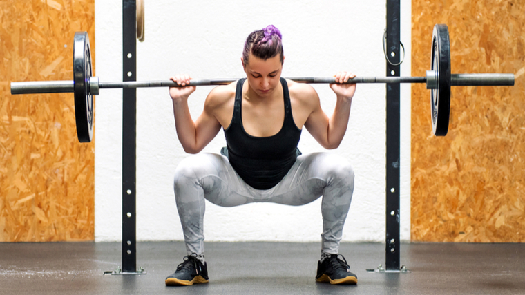 Woman playing barbell squat on a rack