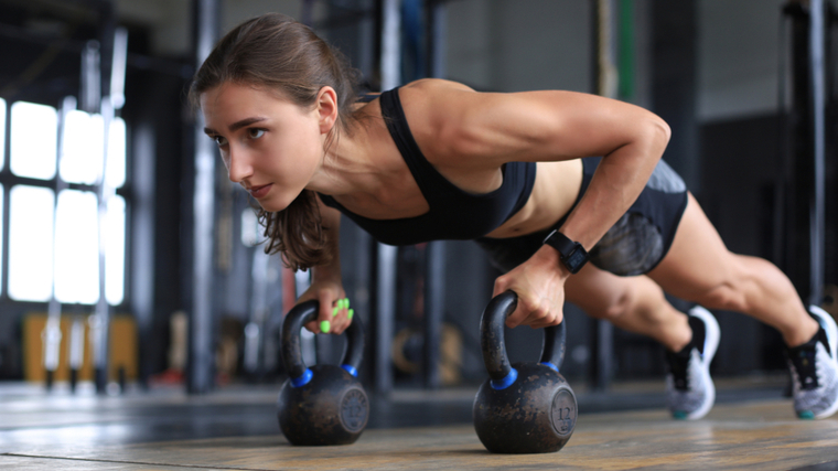 person in push-up position holding kettlbells