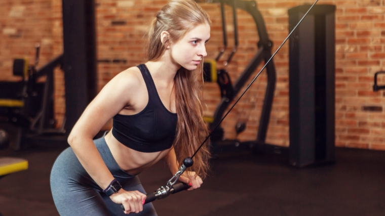 person in gym bent forward holding handle attached to cable