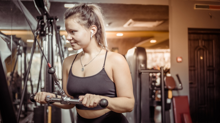 person in gym wearing tank top performing cable triceps exercise