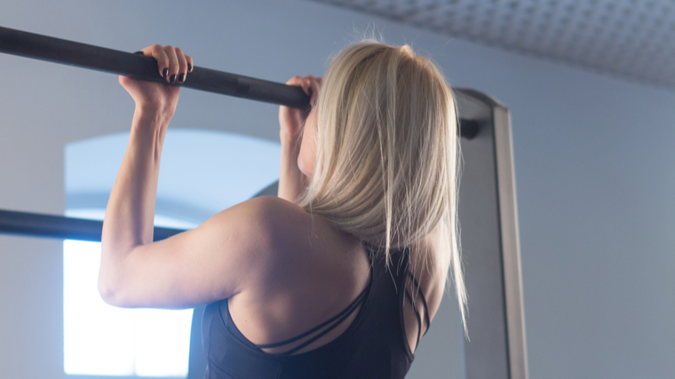 person with long hair in gym performing chin-ups