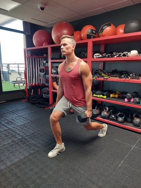 person in gym performing dumbbell lunge