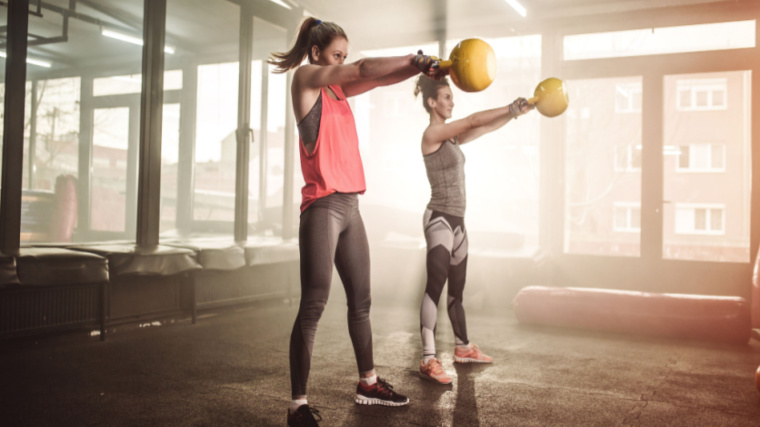 two people in gym performing kettlebell swing