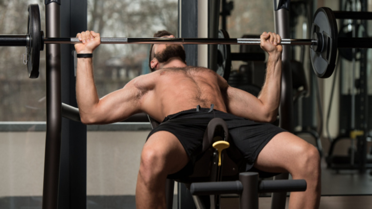 shirtless person in gym performing barbell press