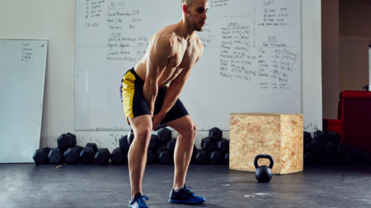 shirtless person in gym performing kettlebell swing