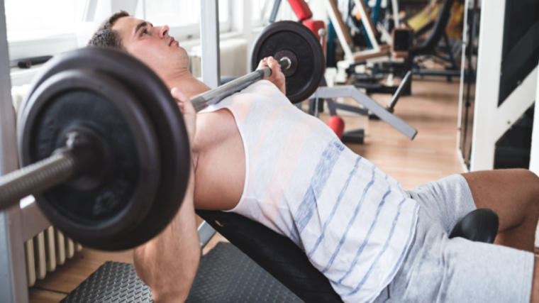 person in gym on bench holding barbell on chest