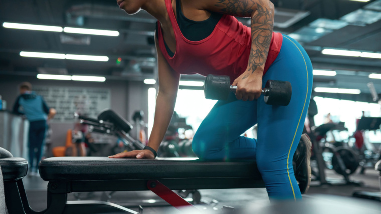 tattooed person doing dumbbell exercise in gym
