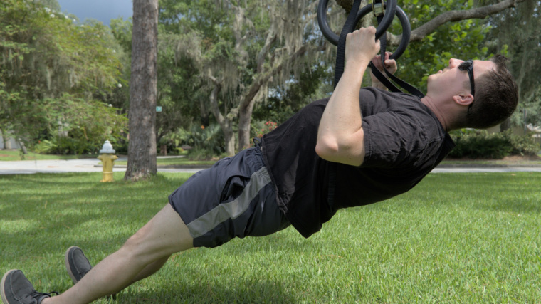 person outdoors doing back exercise on rings