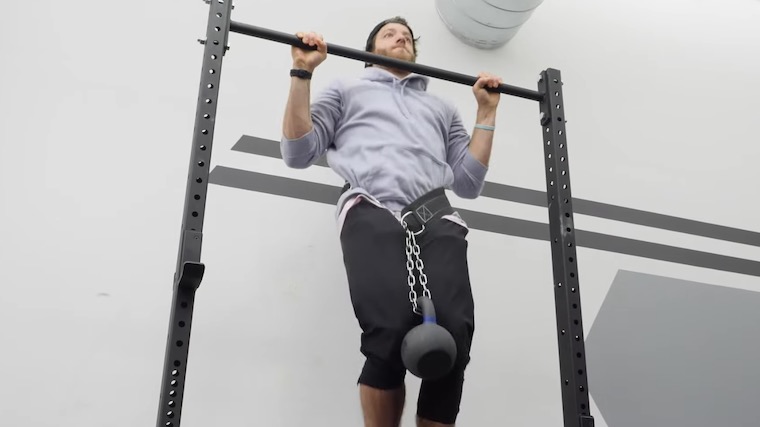 person in gym performing pull-up with weighted belt