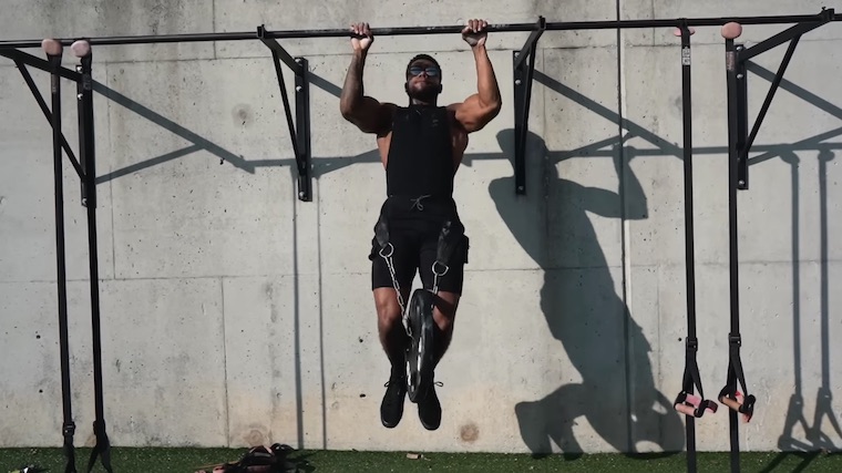 person outdoors doing pull-ups wearing weighted belt
