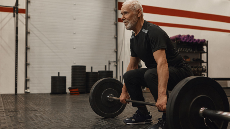grey-haired lifter in gym performing barbell deadlift