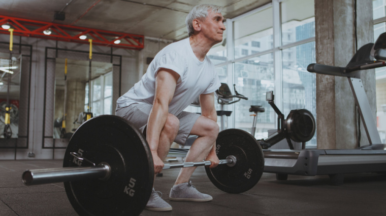Grey-haired person in gym doing barbell deadlift