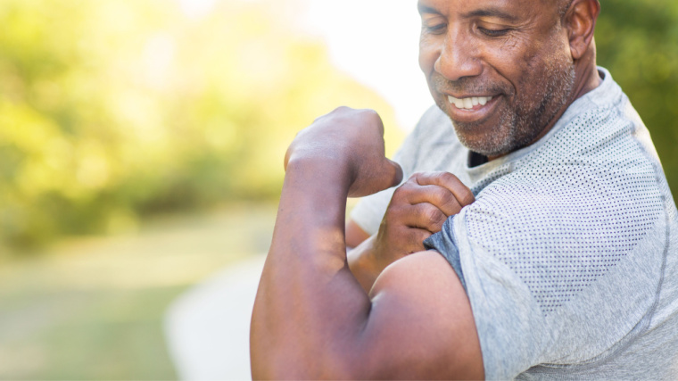 grey-haired person outdoors flexing biceps muscle